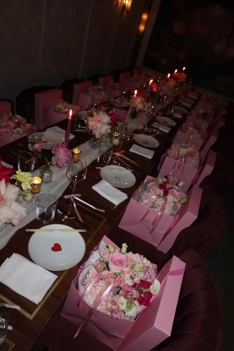 Long candlelit table at Beefbar set for a Galentine’s dinner, featuring pink floral arrangements from @piroflowers and gift boxes from @reve_sleepwear, heart plates, and elegant place settings in NYC.