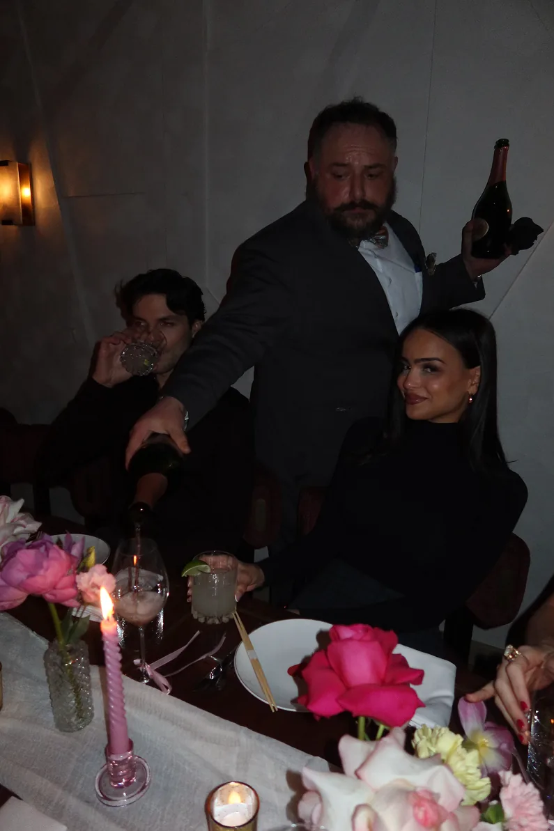 A server pours champagne at a candlelit Galentine’s dinner at Beefbar NYC, as @lisaramos and @philipp.davis enjoy cocktails, roses, and an intimate celebration setting.