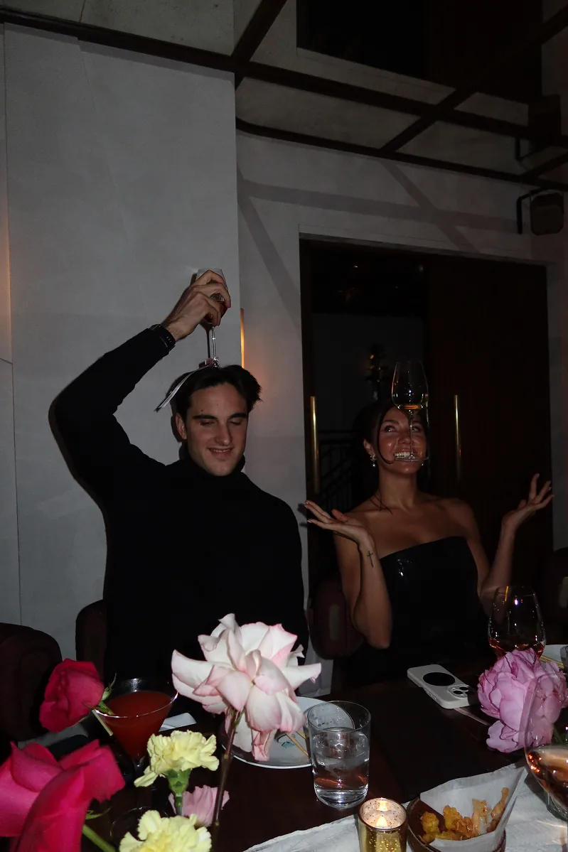@theeuropeankid and @catafreer playfully balance wine glasses during a candlelit Galentine’s dinner at Beefbar NYC, surrounded by pink roses, cocktails, and an intimate tablescape.