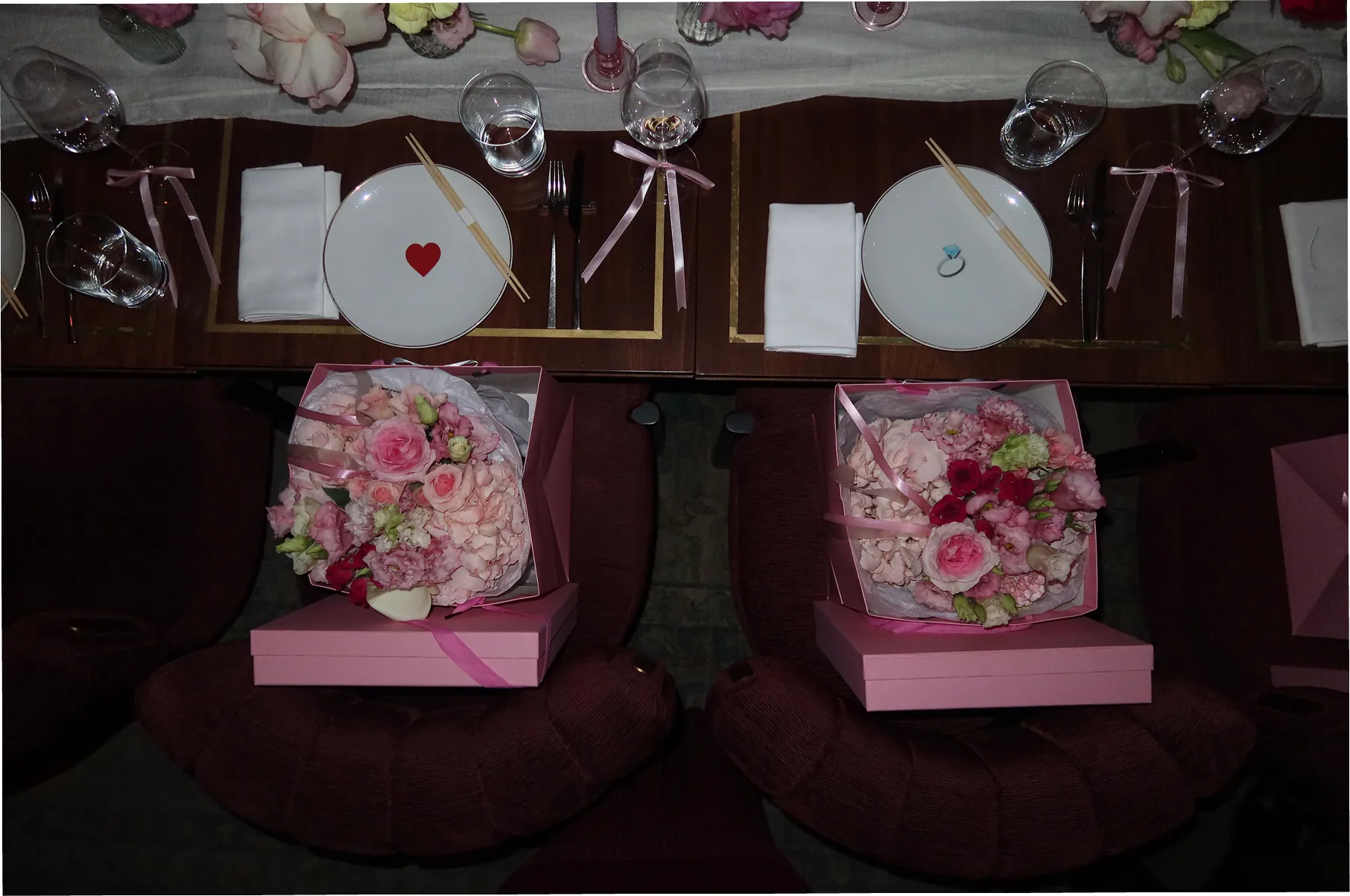 Overhead view of a candlelit Galentine’s Dinner table at Beefbar NYC, featuring pink floral bouquets from @piroflowers and gift boxes from @reve_sleepwear , white plates with heart details, ribbon-tied napkins, and elegant place settings.