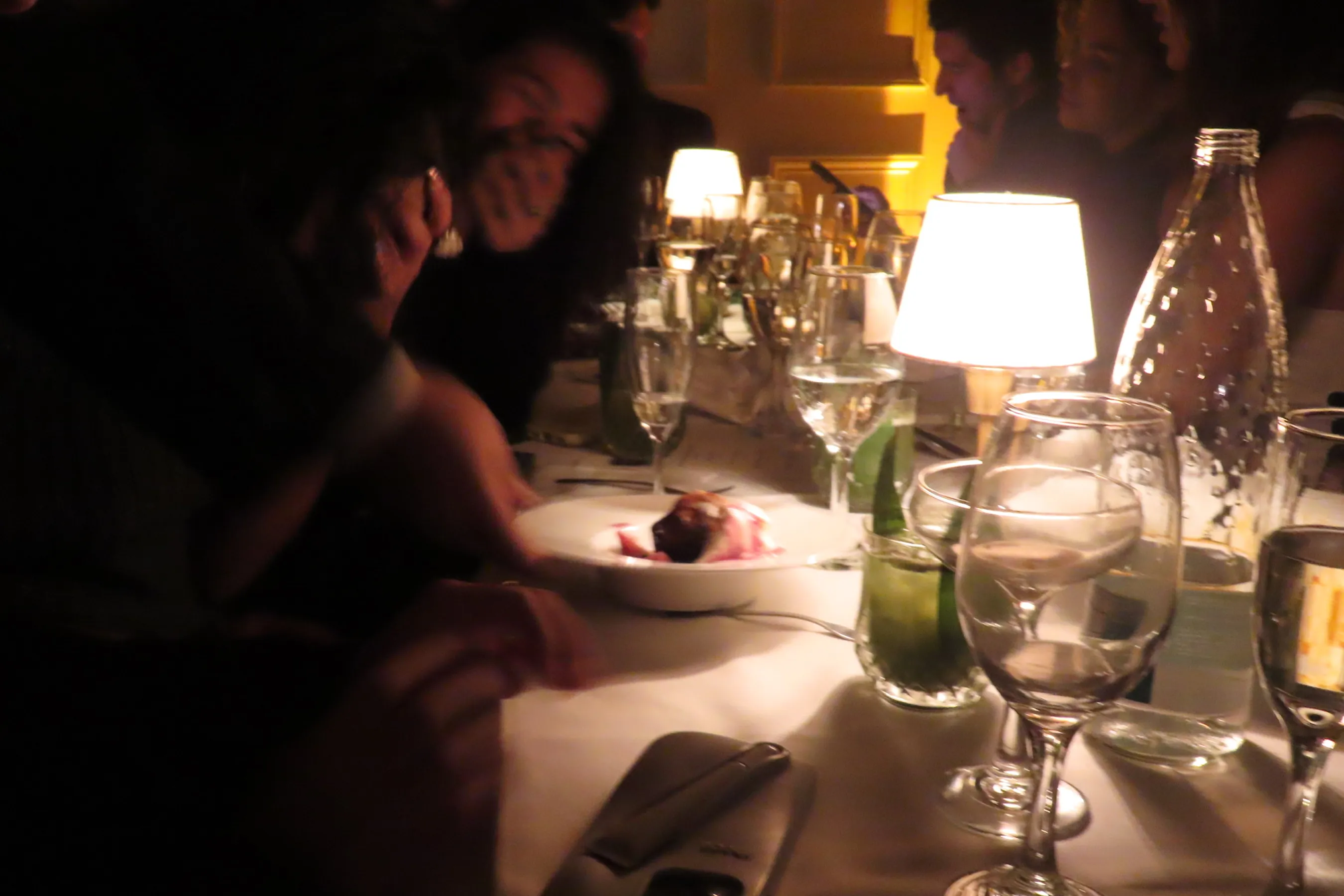 Guests gathered around a candlelit dinner table enjoying a plated dessert, surrounded by glowing table lamps, wine glasses, and elegant place settings. The warm, intimate lighting captures the cozy, upscale atmosphere of the Storytime evening at Déjà Vu.