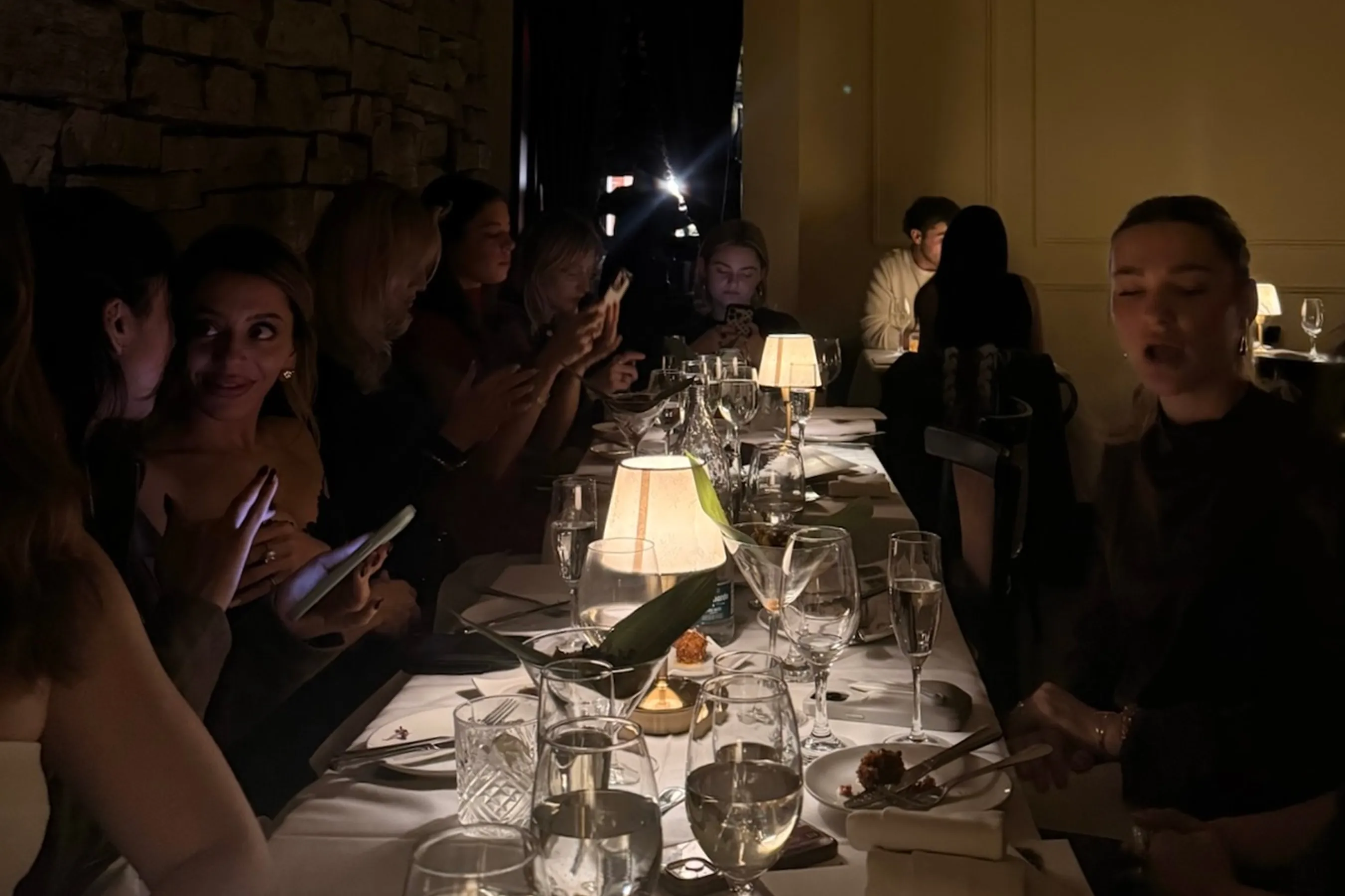 A long candlelit dinner table filled with elegantly dressed guests, glowing table lamps, wine glasses, and plated courses. Creators gather in an intimate, dimly lit setting, capturing content and enjoying conversation during the Storytime dinner at Déjà Vu.