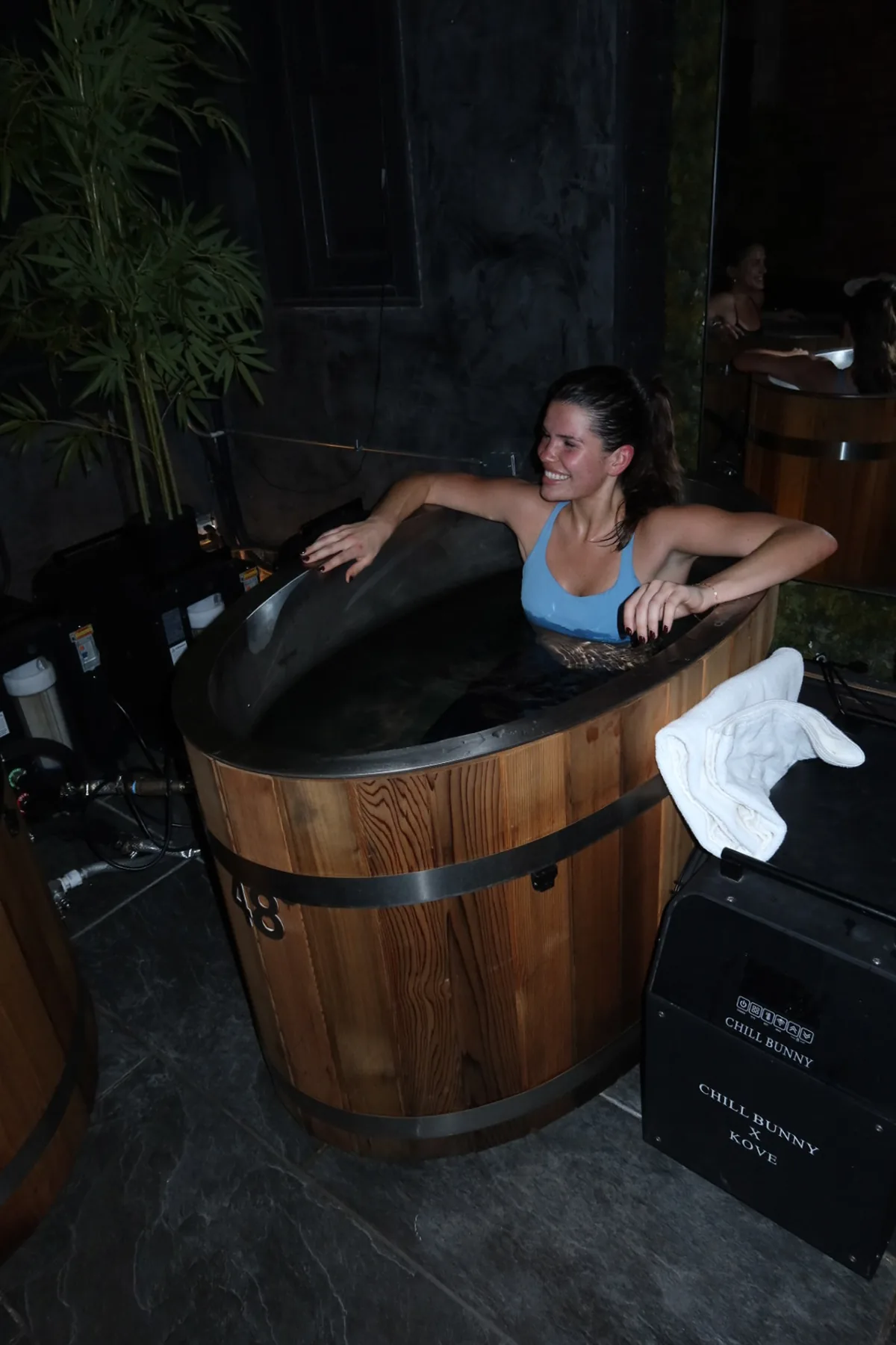 A Storytime Influencer relaxes in a wooden cold plunge tub from @chillbunny_wellness at Kove Studio during the Wellness Reset Event. The dim, spa-like setting and recovery equipment highlight the focus on cold therapy and post-workout rejuvenation.