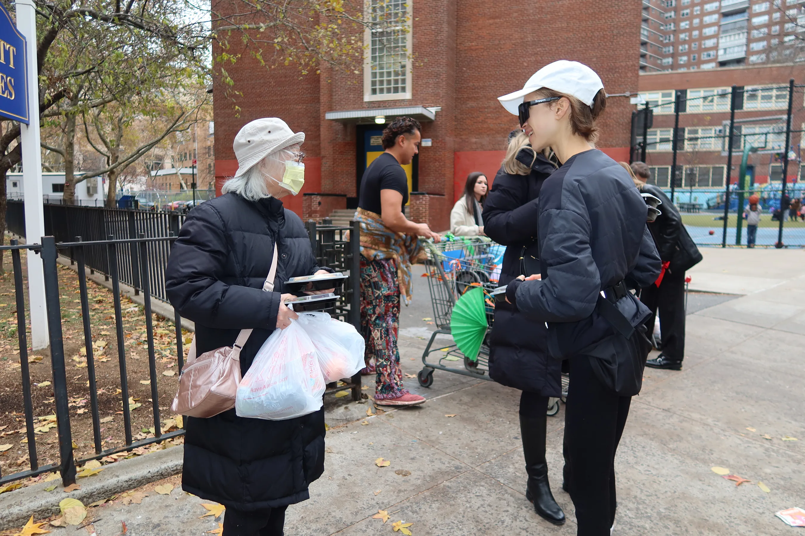 A Storytime creator speaks with an elderly woman receiving Thanksgiving meal packages during The Migrant Kitchen Initiative distribution event in a New York neighborhood.