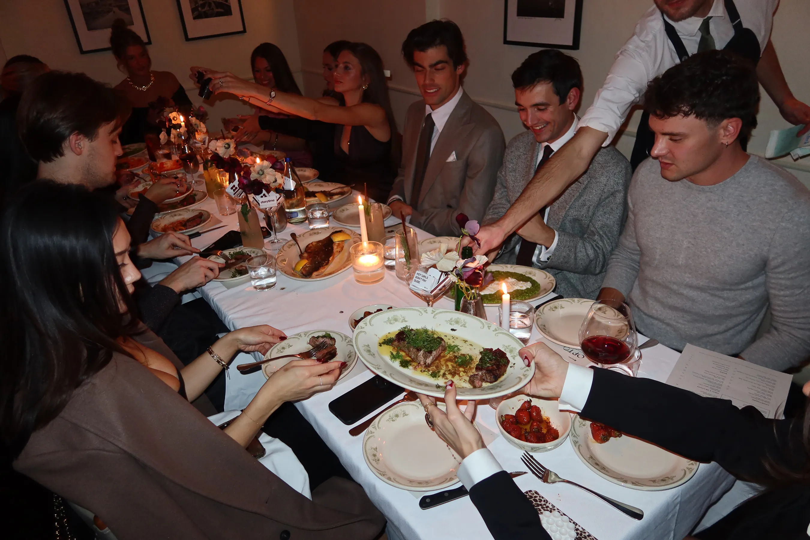 @thequeenfoodie @everythingebbie @ellieforthegirls @jessworkk @evitascoccia @madsmaley @itslaurenraymond @treed_fl @samnoyer @rachelgracewilson @nycfoodfaves @andrewpolo_ @elliottdurprey @allinaaai @vito_999 @_taniagrover @dishingdaily @boujeebitesonly @katie.overholt @williamjackman2 and @jakeeldridge_ sitting at A long dinner table at Opto filled with Storytime creators sharing a Friendsgiving-style meal. Guests are dressed elegantly, passing plates of steak and vegetables across the table while candles, floral arrangements from @apartment.387, and vintage-style plates create a warm, intimate atmosphere.