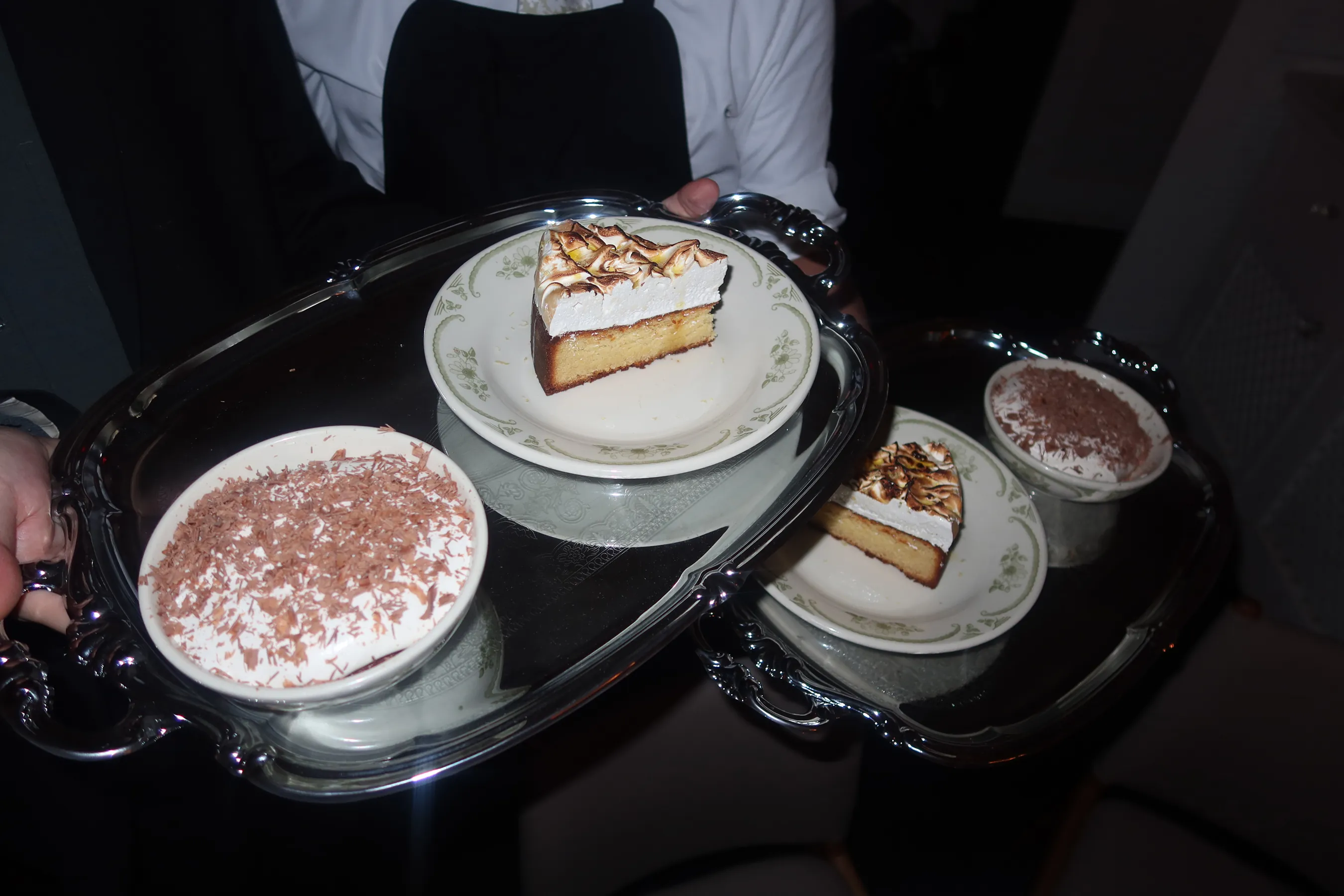 A server presents silver trays featuring slices of Opto almond meringue cake and chocolate mousse during the Storytime Friendsgiving dinner at Opto.