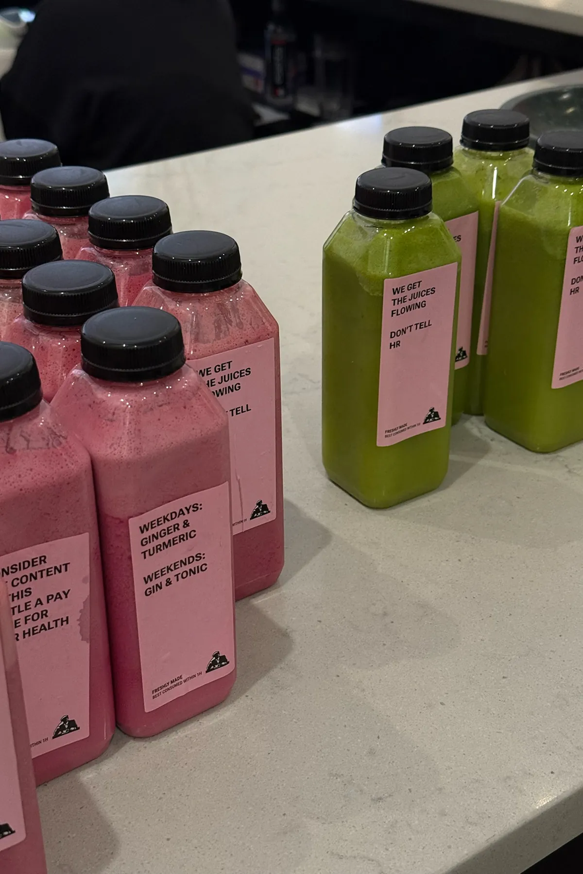 Joe and The Juice pink and green bottled juices with minimalist labels arranged on a countertop, featuring playful text.