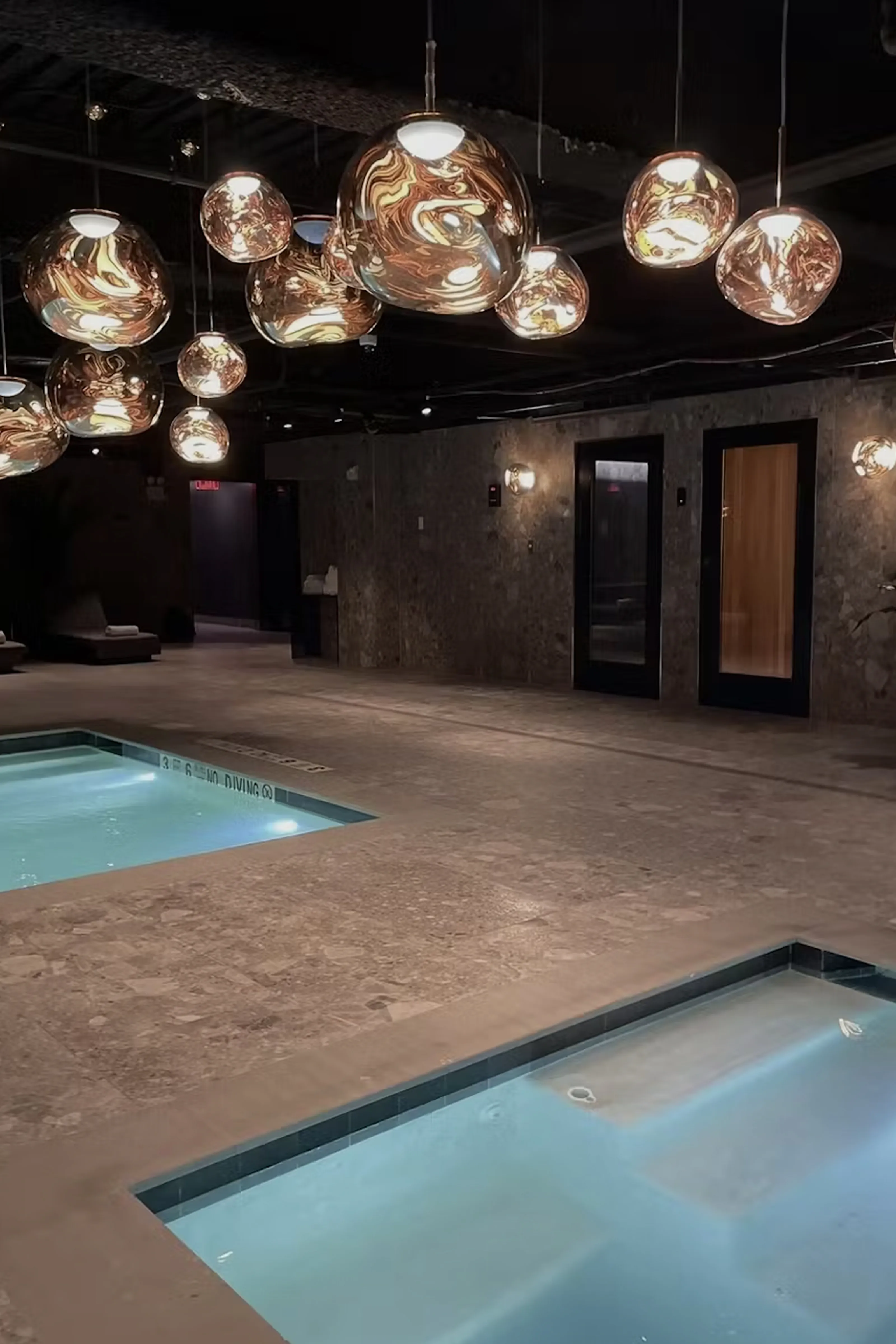 TMPL Club’s luxury spa area featuring illuminated plunge pools, modern stone flooring, and sculptural metallic pendant lights, highlighting the gym’s upscale recovery amenities and serene, high-end atmosphere.