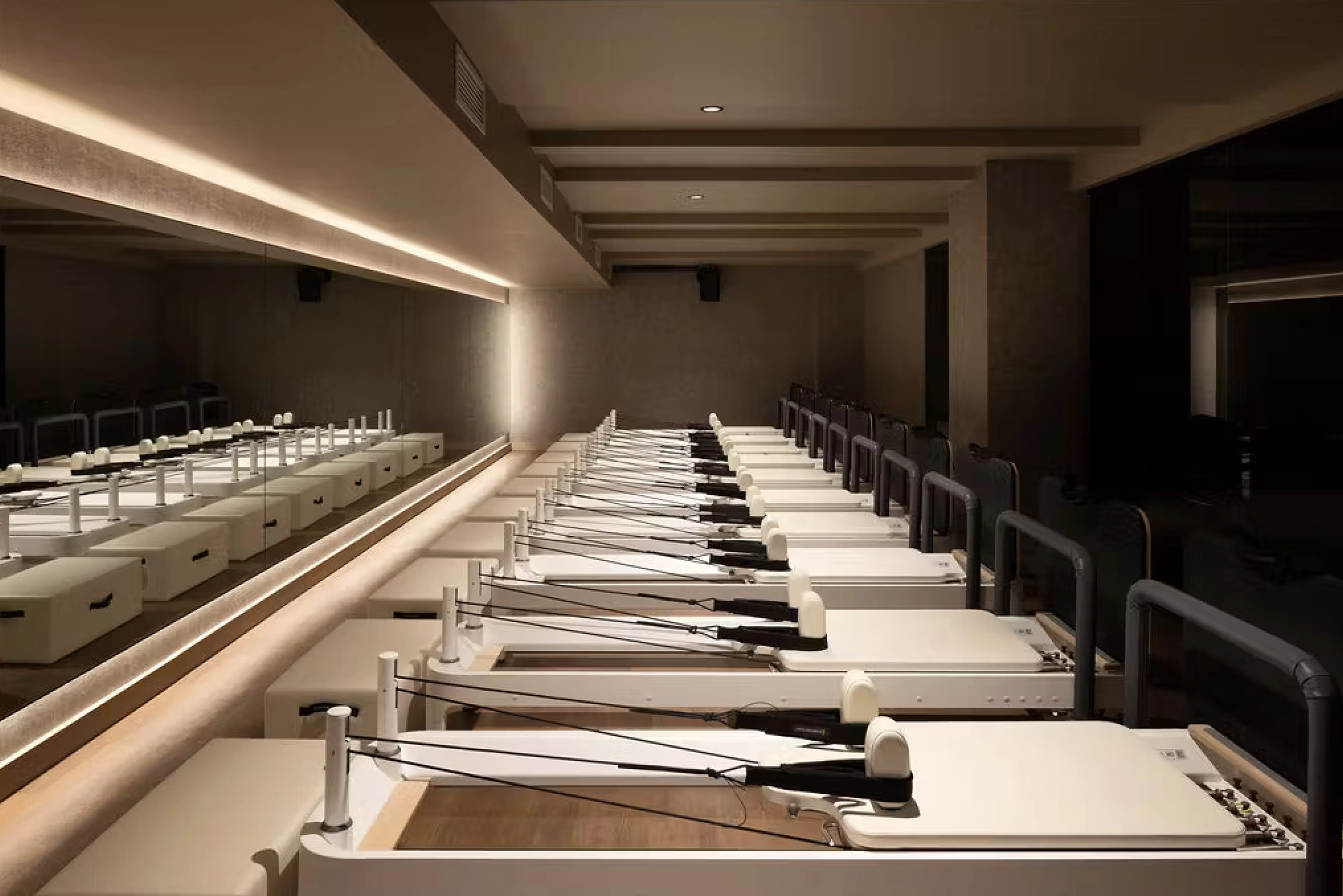 A sleek, modern Pilates studio at TMPL Club featuring a row of premium reformer machines, warm ambient lighting, and minimalist design details, reflecting the gym’s upscale and refined wellness experience.