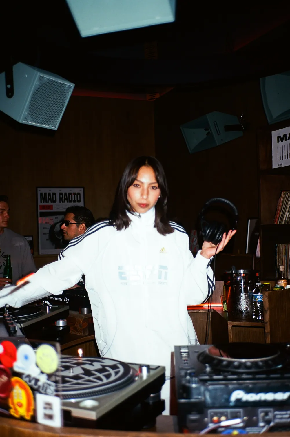 Guest DJ wearing a white ESM tracksuit holds headphones during a live music set at a Storytime event in NYC.