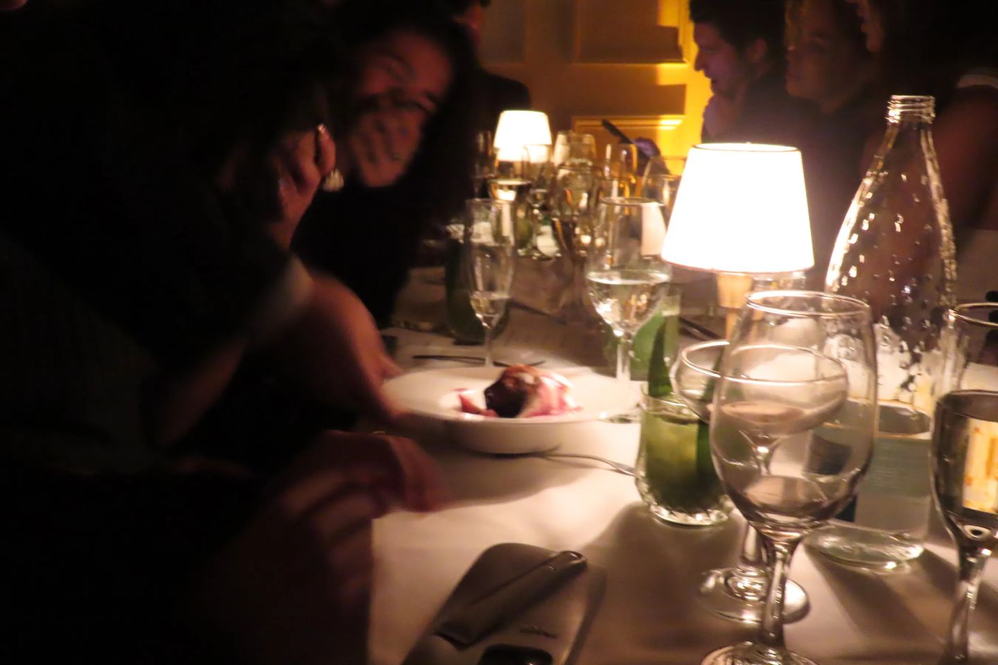 Guests gathered around a candlelit dinner table enjoying a plated dessert, surrounded by glowing table lamps, wine glasses, and elegant place settings. The warm, intimate lighting captures the cozy, upscale atmosphere of the Storytime evening at Déjà Vu.