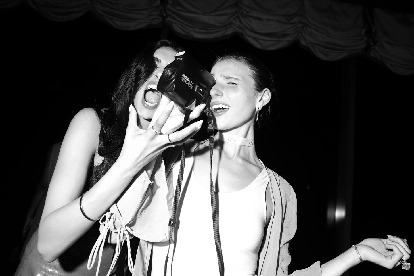 Black and white candid of two women laughing with a vintage film camera at the Made in New York party in NYC.