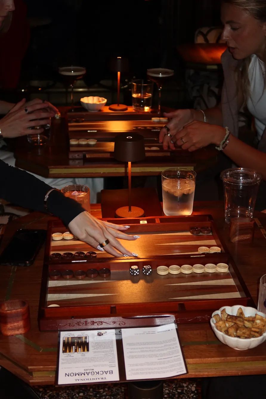 Guests play backgammon over drinks and snacks during the Storytime x Backgammon Social event at Beefbar NYC in a candlelit lounge setting.