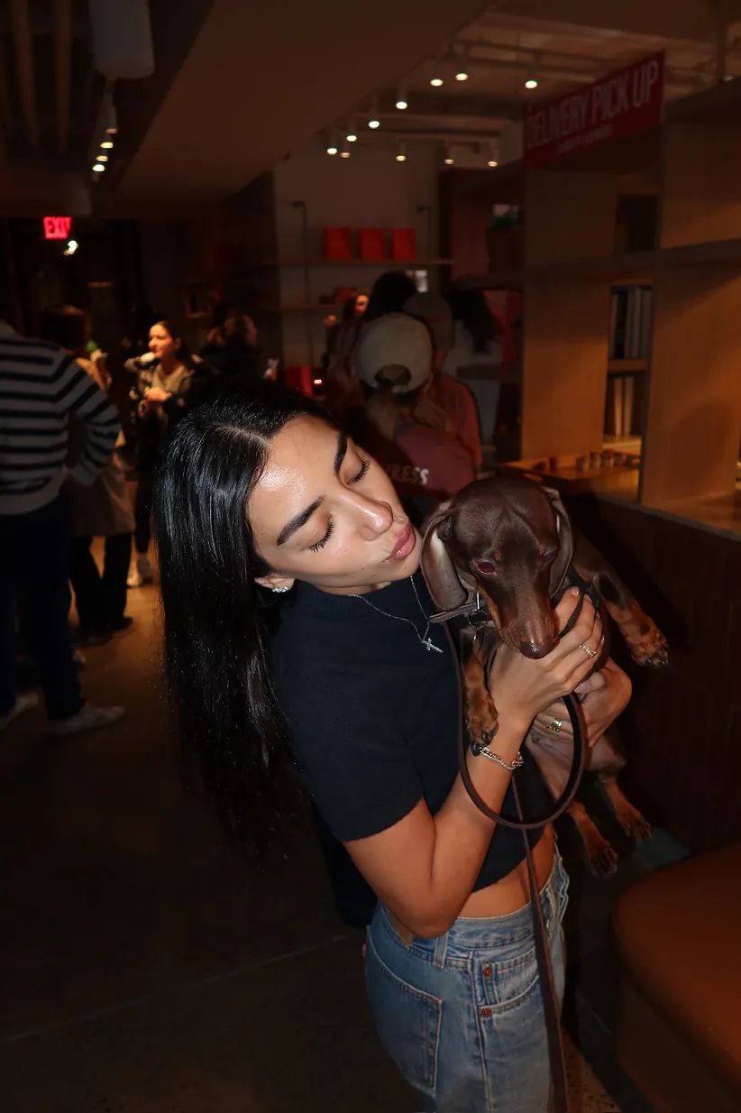 A guest holds a dachshund during the Storytime celebration at the new Carrot Express NoLita opening, as attendees mingle inside the NYC café space.