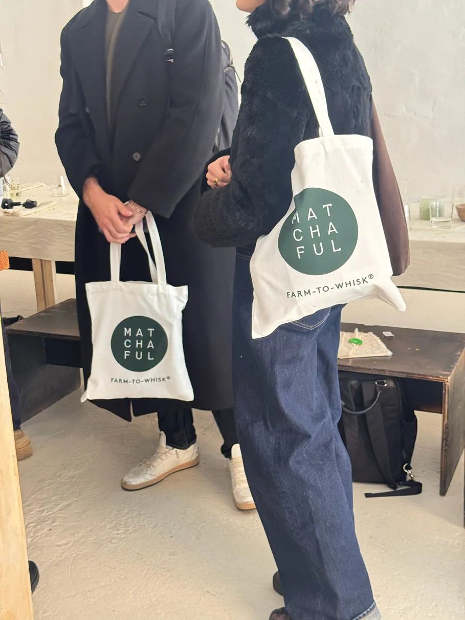 Guests at a Matchaful x Storytime event carry branded Matchaful tote bags while mingling inside a minimalist event space after a matcha tasting experience.