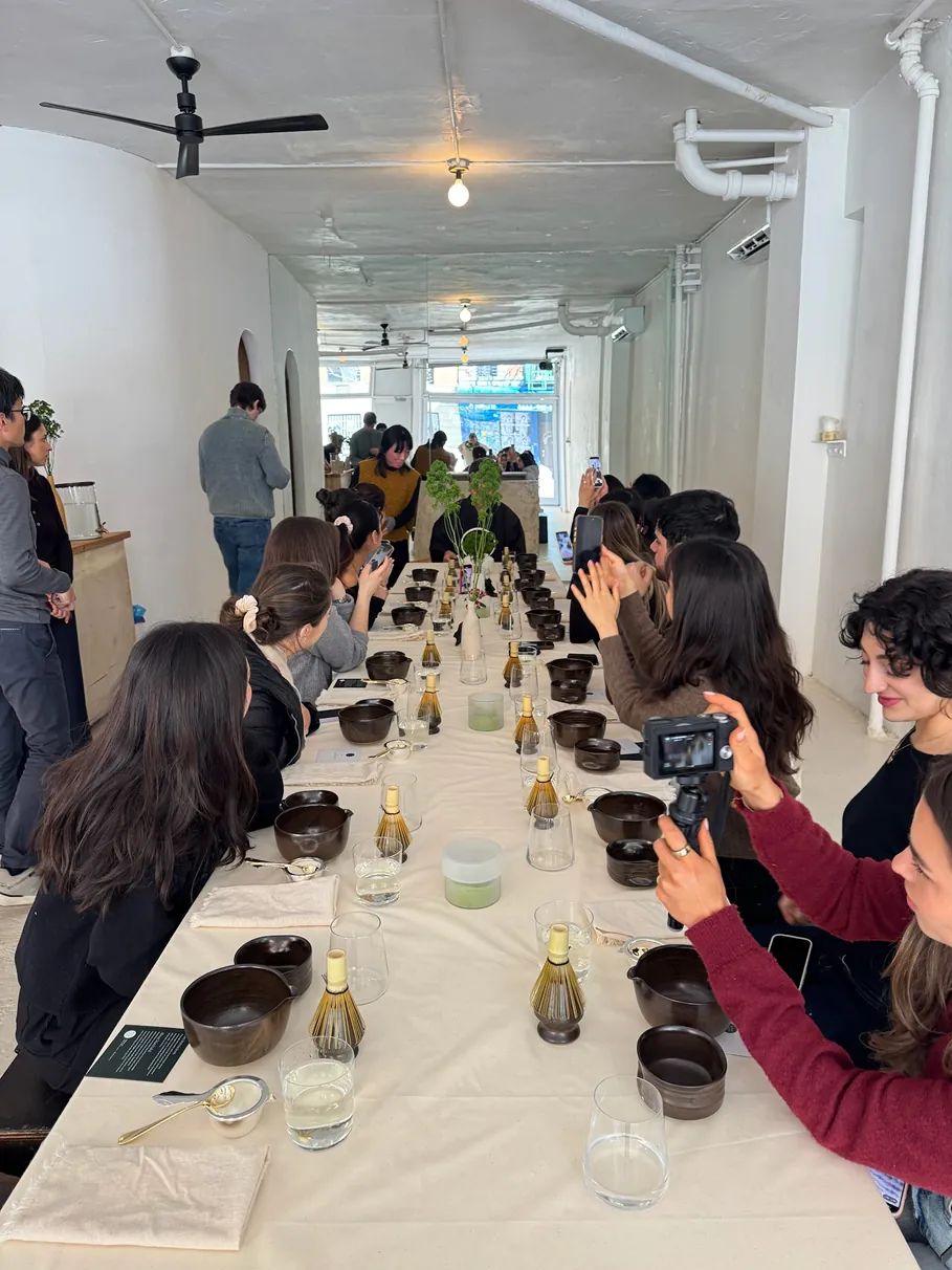 Storytime creators gather around a long communal table during a Matchaful workshop, documenting the experience while learning traditional matcha preparation in a minimalist NYC studio.