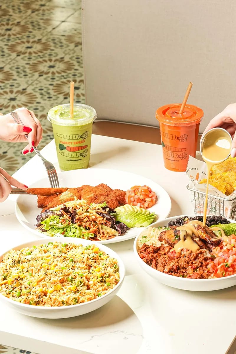 Overhead Carrot Express breakfast spread with a quinoa egg bowl, radish avocado toast, scrambled egg plate, and red cold-pressed juice in an orange-lidded cup