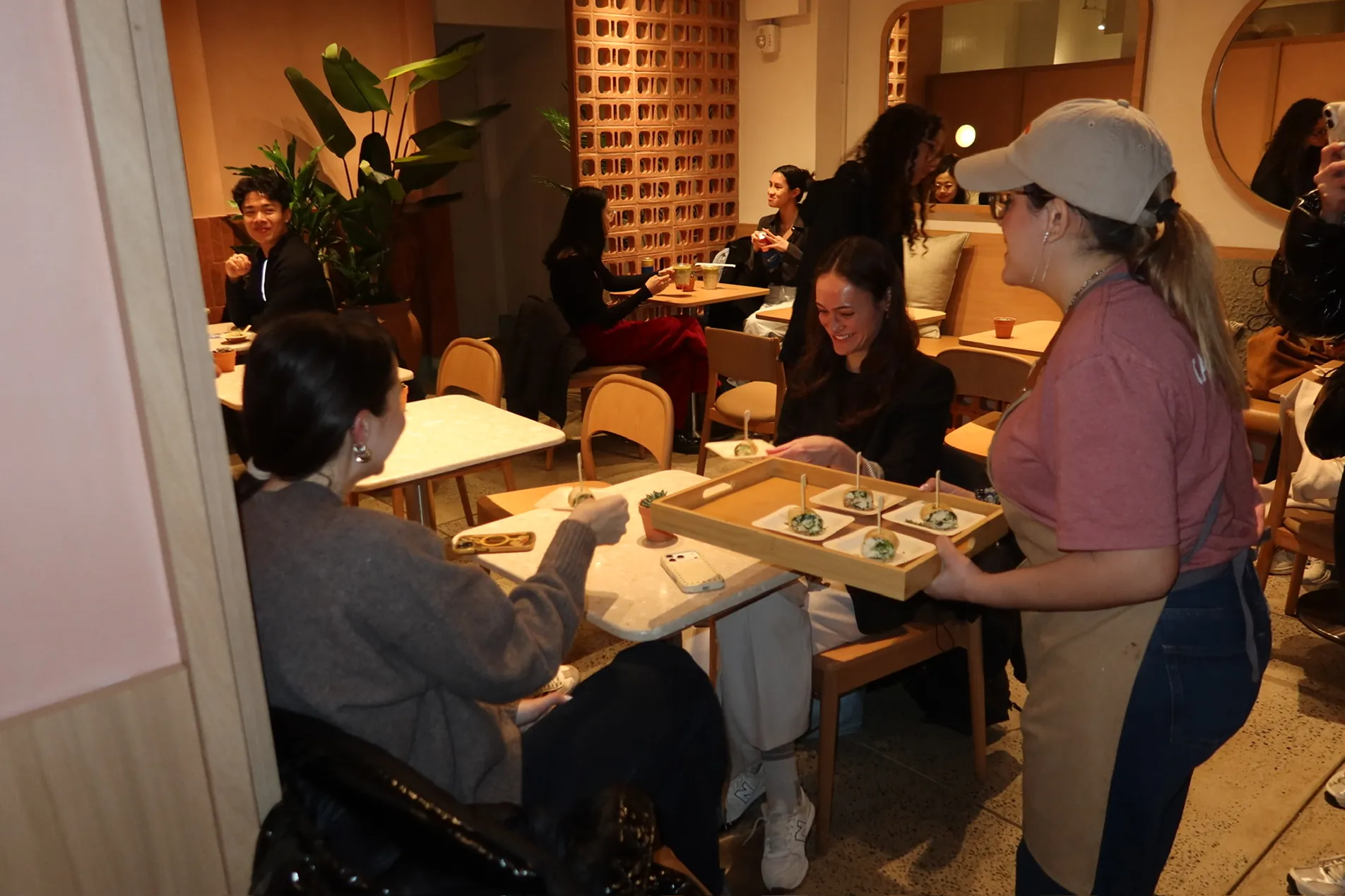 Guests gather and enjoy bites during the Storytime celebration at the new Carrot Express NoLita location, as staff serve food and drinks in the warm café space.