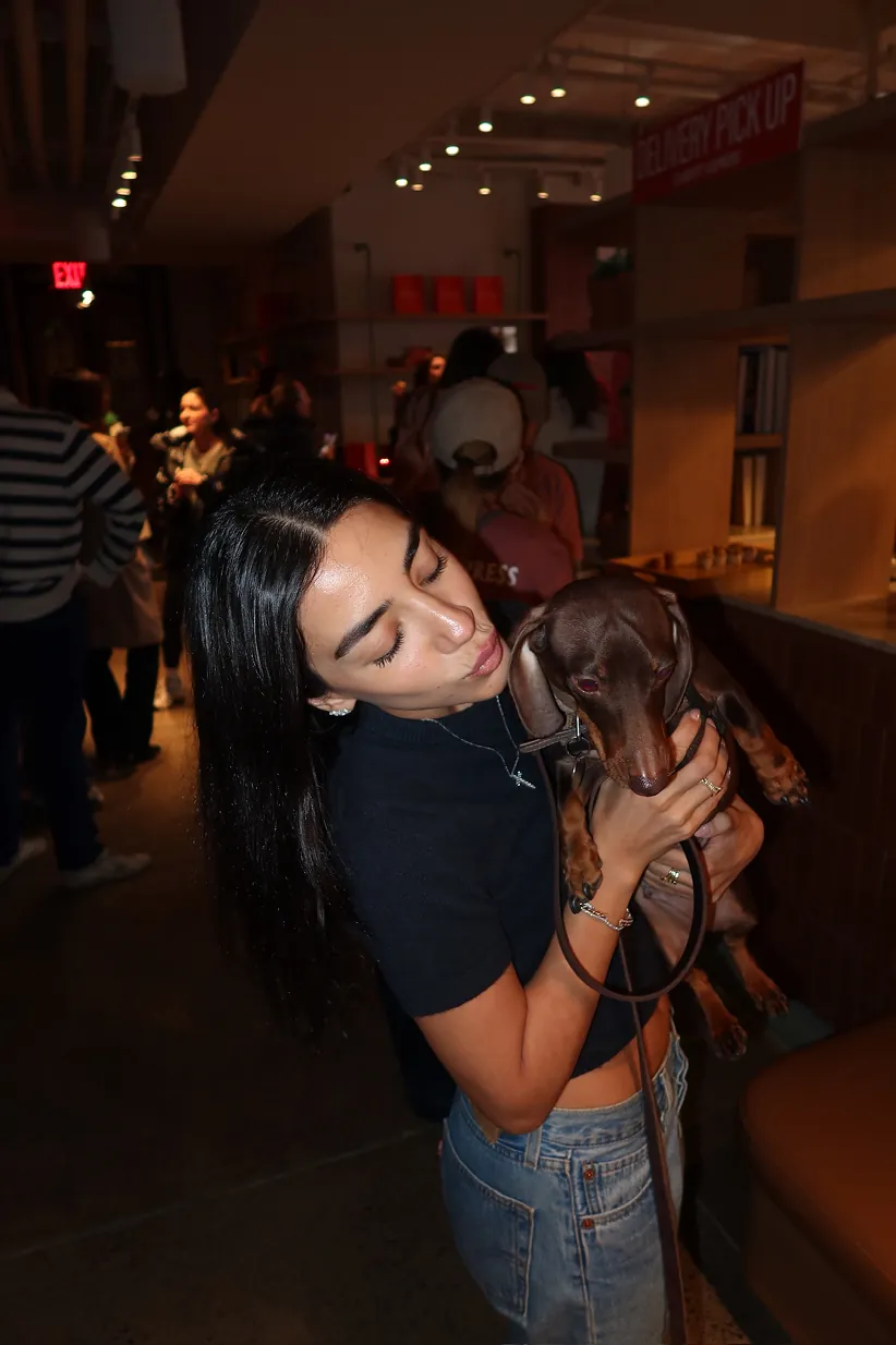 A guest holds a dachshund during the Storytime celebration at the new Carrot Express NoLita opening, as attendees mingle inside the NYC café space.